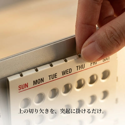 曜日カード上辺の切り欠きに指をかけて、プレートに掛けるところのマクロ写真。