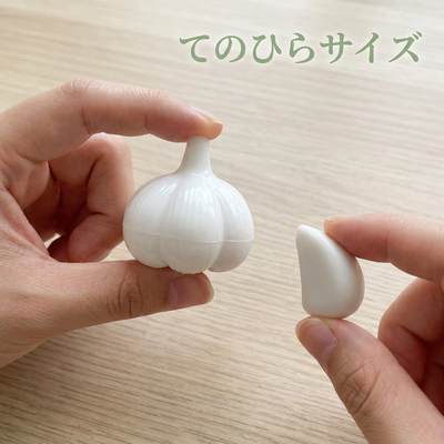 指先でつまめるてのひらサイズ。白いにんにく型消しゴムと粒を手に持つ様子